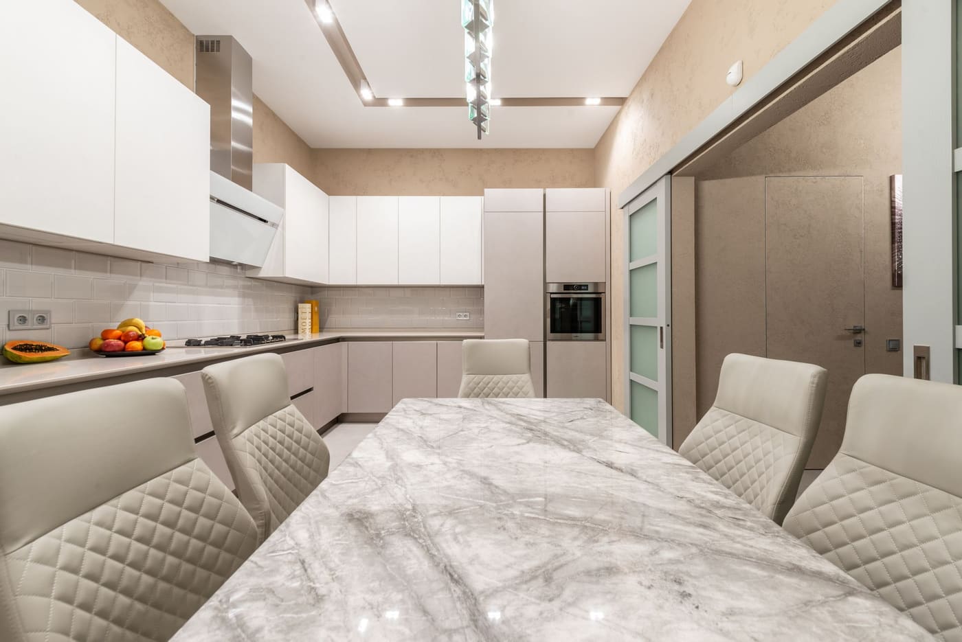 A calm beige kitchen with a marble table and sculptural pendant